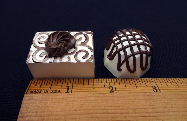 Two fake chocolate candies, one with a swirl design and the other with a lattice design, are shown next to a ruler. The candies are approximately 1 inch in size.