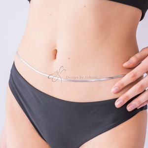 May include: A silver body chain worn around the waist. The chain is thin and delicate, resting just above the black underwear. The image includes the text "Design by Athena".