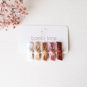 May include: Set of six velvet hair clips in various colours, including white, beige, brown, pink, and red. The clips are arranged on a white card with the text "bambi lane hair accessories".