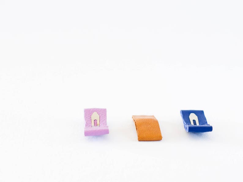 May include: Three leather tags with metal clasps. The tags are pink, orange, and blue.