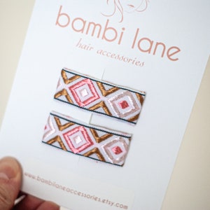 Könnte beinhalten: Zwei rosafarbene und goldfarbene Haarklammern mit Muster auf weißem Hintergrund. Die Klammern befinden sich auf einer weißen Karte mit dem Text "bambi lane hair accessories" und "www.bambilane.accessories.etsy.com".