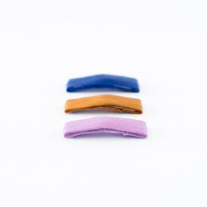 May include: Three leather straps in different colors: blue, brown, and purple. The straps are arranged vertically, with the blue strap at the top and the purple strap at the bottom.