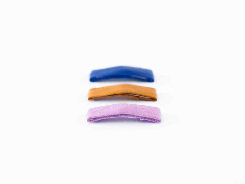 May include: Three leather straps in different colors: blue, brown, and purple. The straps are arranged vertically, with the blue strap at the top and the purple strap at the bottom.