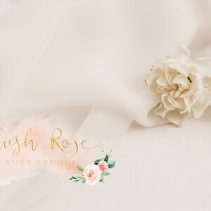 Puede incluir: Un fondo suave de color crema con una delicada flor blanca y el texto "Blush Rose BEAUTY STUDIO" en escritura dorada. El logotipo presenta un toque de acuarela rosa y melocot&oacute;n con detalles florales.