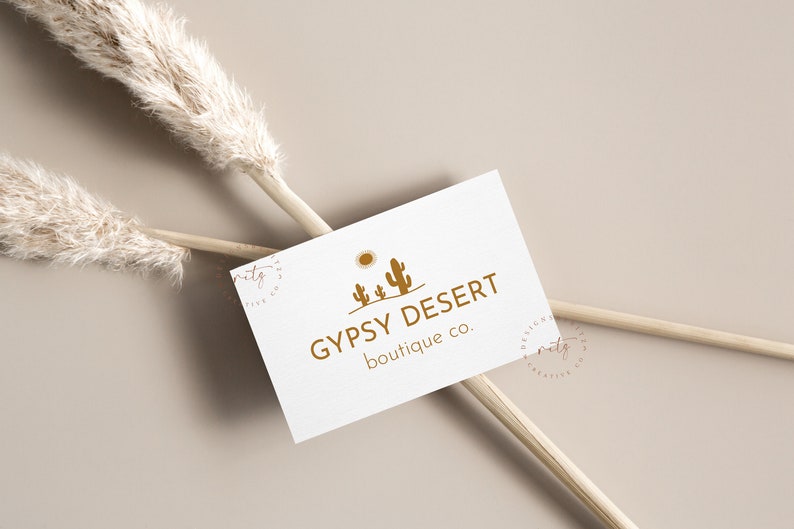 May include: A white business card with a logo of a desert scene with a sun and three cacti in brown. The text "GYPSY DESERT boutique co." is printed in brown below the logo.