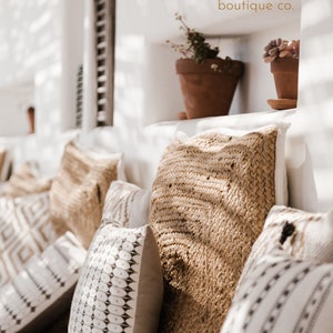 May include: A collection of throw pillows with various patterns and textures. The pillows are arranged on a white couch with a white wall behind them. The pillows are made of a variety of materials, including woven fabric and cotton. The pillows are in a variety of colors, including white, brown, and black. The pillows are arranged in a way that creates a sense of comfort and relaxation. The text "GYPSY DESERT boutique co." is visible in the top right corner of the image.