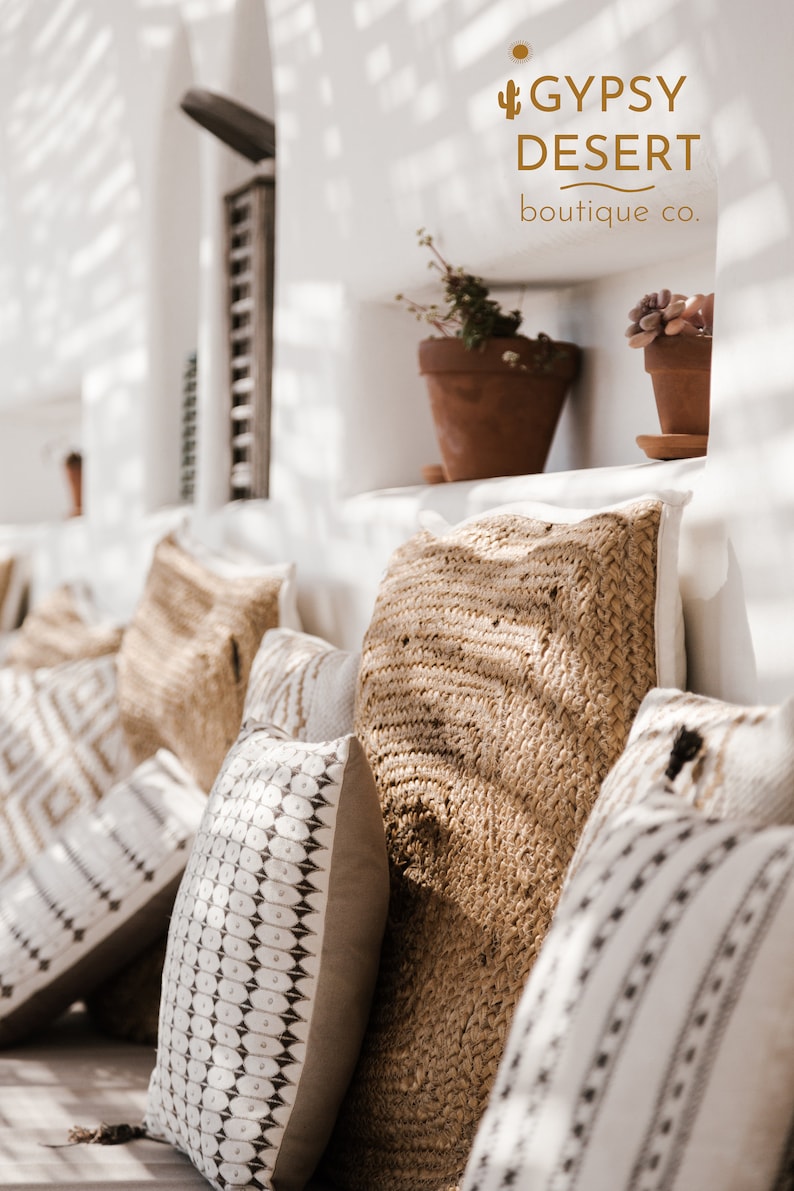 May include: A collection of throw pillows with various patterns and textures. The pillows are arranged on a white couch with a white wall behind them. The pillows are made of a variety of materials, including woven fabric and cotton. The pillows are in a variety of colors, including white, brown, and black. The pillows are arranged in a way that creates a sense of comfort and relaxation. The text "GYPSY DESERT boutique co." is visible in the top right corner of the image.