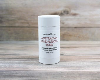 May include: White deodorant stick with the text "Naturistic Australian Sandalwood Rose Natural Deodorant Baking Soda Free Net wt. 2.6 oz."