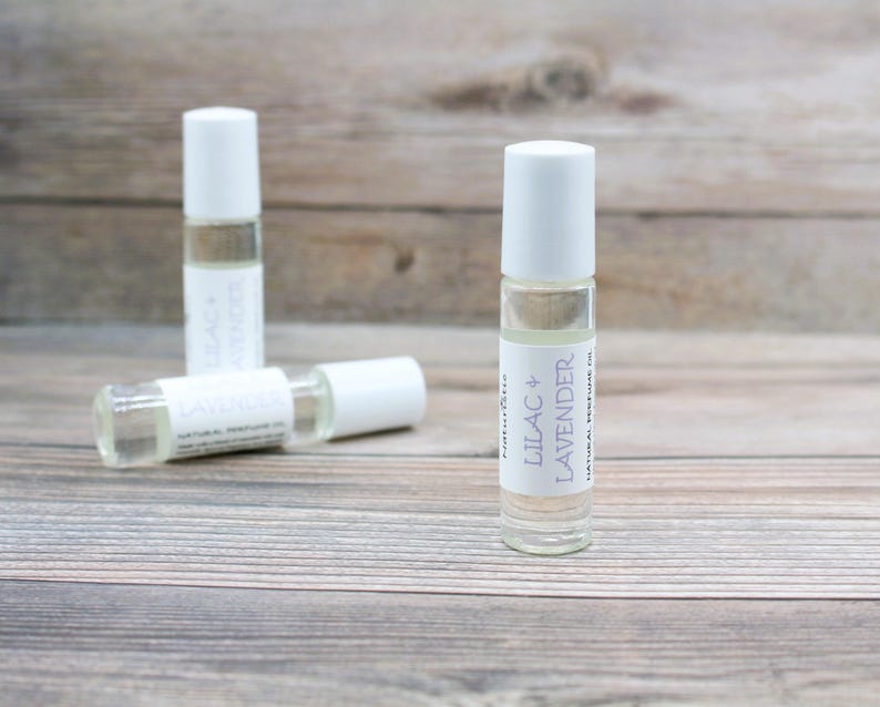 May include: Three glass roller bottles with white caps and labels. The label on the front bottle reads "Lilac & Lavender Natural Perfume Oil".