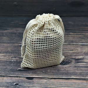 May include: A white mesh produce bag with a drawstring closure. The bag is empty and is sitting on a wooden surface.