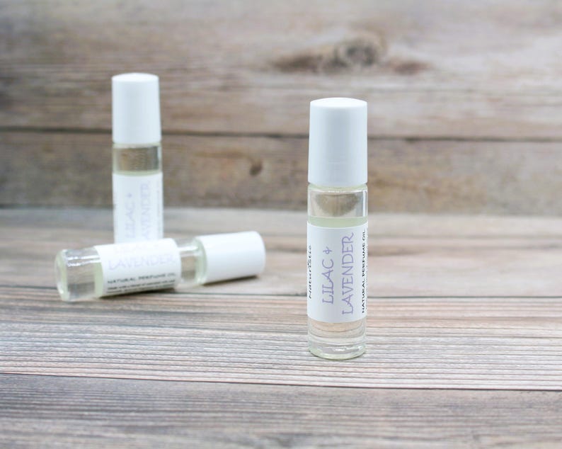 May include: Three white roller bottles with clear liquid inside. The bottle in the center has a label that reads "Lilac + Lavender Natural Perfume Oil".