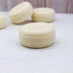 May include: Four white solid shampoo bars on a white surface. The bars are round and have a smooth texture.