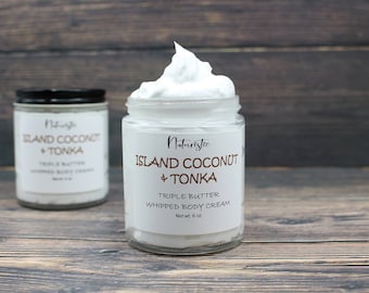 May include: Two glass jars of whipped body cream with white lids. The jars are labeled "Island Coconut + Tonka" and "Triple Butter Whipped Body Cream, Net wt. 6 oz."