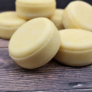 May include: Five round, white, solid shampoo bars on a wooden surface.