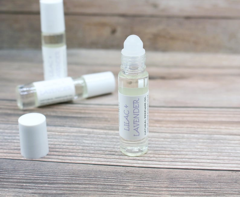 May include: A clear glass roller bottle with a white cap and a white label that reads "Lilac & Lavender Natural Perfume Oil".