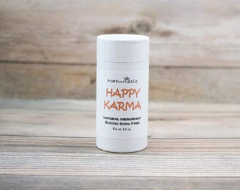 May include: White deodorant stick with the text "Naturistc Happy Karma Natural Deodorant Baking Soda Free Net wt. 2.6 oz."