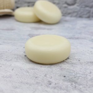 May include: Three round, white, solid shampoo bars on a light gray textured surface.
