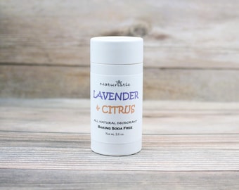 May include: A white deodorant stick with the text "Lavender + Citrus" in purple and orange. The label also reads "All Natural Deodorant Baking Soda Free" and "Net wt. 2.6 oz.". The product is on a light wood background.