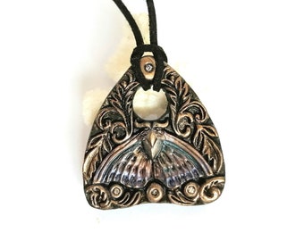 May include: A triangular pendant necklace with a black cord. The pendant is made of metal and features a detailed design of a butterfly with wings in shades of blue, purple, and green. The pendant is accented with small, clear rhinestones.