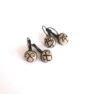 May include: A pair of earrings with a bronze finish and white ceramic round beads. Each bead has a black geometric design.