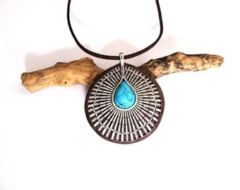 May include: A turquoise stone pendant necklace with a silver and brown circular design. The necklace is hanging from a brown leather cord.