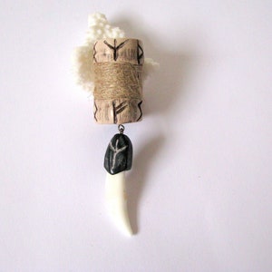 May include: A wooden pendant with a carved design and a black stone charm hanging from it. The pendant is attached to a white crocheted cord.