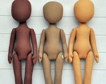 May include: Three fabric dolls standing in a row. The doll on the left is brown, the middle doll is beige, and the doll on the right is light brown.