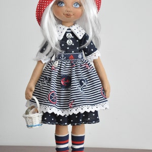 May include: A handmade doll wearing a blue and white striped dress with nautical themed prints, a red and white polka dot hat, and red and white striped socks. The doll is holding a white wicker basket.