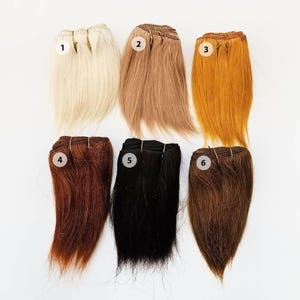 May include: Six bundles of hair extensions in various colours: blonde, light brown, golden, auburn, black, and dark brown. Each bundle is secured with a weft and labelled with a number.
