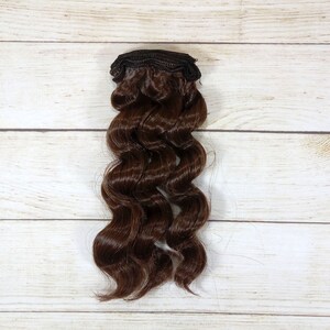 Puede incluir: Una extensi&oacute;n de cabello ondulado marr&oacute;n con un clip de sujeci&oacute;n.