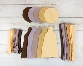 May include: An overhead shot displays a collection of fabric pieces in various shapes and colors. There are several sets of cut fabric pieces in shades of brown, lavender, and beige. The pieces are arranged on a light-colored wooden surface.