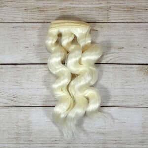 Puede incluir: Una trama de extensiones de cabello humano ondulado, rubio platino.