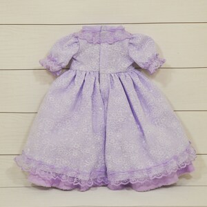 K&ouml;nnte beinhalten: Ein lavendelfarbenes Kleid mit Blumenmuster und Spitzenbesatz. Das Kleid hat einen hohen Kragen und kurze &Auml;rmel.