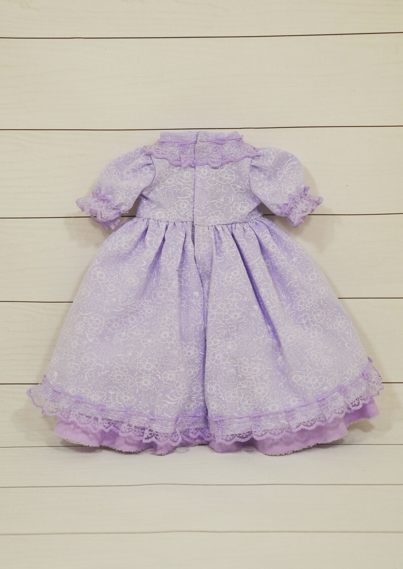 K&ouml;nnte beinhalten: Ein lavendelfarbenes Kleid mit Blumenmuster und Spitzenbesatz. Das Kleid hat einen hohen Kragen und kurze &Auml;rmel.