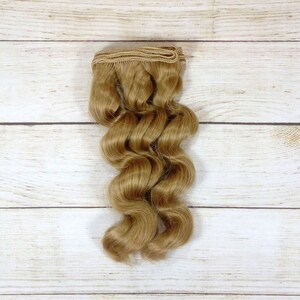 Puede incluir: Una trama de extensiones de cabello humano ondulado, rubio claro.