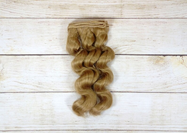 Puede incluir: Una trama de extensiones de cabello humano ondulado, rubio claro.
