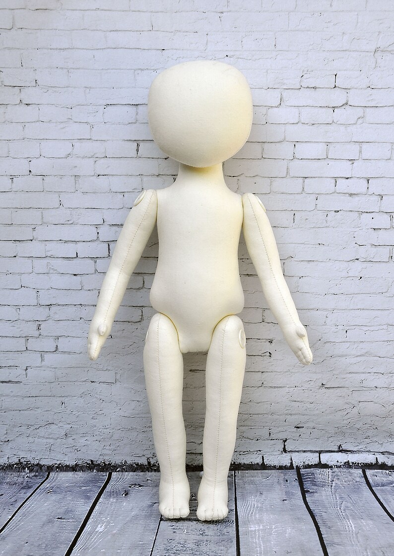 K&ouml;nnte beinhalten: Eine wei&szlig;e Stoffpuppe mit beweglichen Armen und Beinen. Die Puppe steht auf einem Holzboden vor einer wei&szlig;en Backsteinwand.