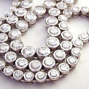 May include: A silver necklace with multiple rows of round, clear stones. The stones are set in a bezel setting and are of varying sizes.