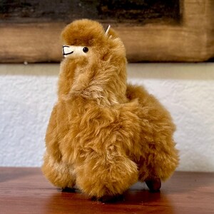 Op de afbeelding: Een bruin alpaca knuffeldier met een pluche textuur. Het speelgoed staat op een houten oppervlak.