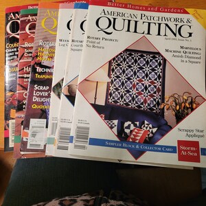 Könnte beinhalten: Ein Stapel von acht American Patchwork & Quilting-Magazinen mit bunten Covern, die Quiltmuster und -projekte zeigen. Das oberste Magazin trägt den Titel "American Patchwork & Quilting" mit dem Untertitel "Marvelous Machine Quilting: Amish Diamond in a Square".