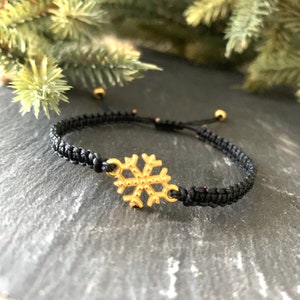 May include: A black braided bracelet with a gold snowflake charm.