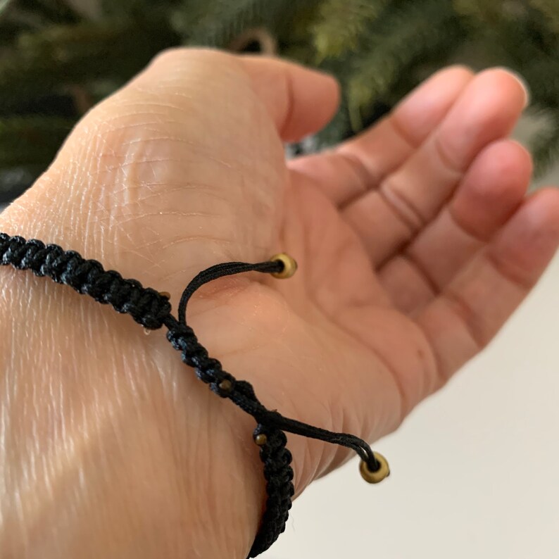 May include: A black adjustable bracelet with gold metal beads and a sliding knot closure.
