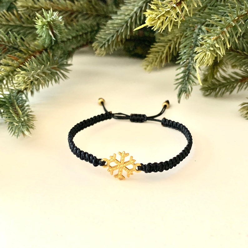 May include: A black adjustable cord bracelet with a gold snowflake charm.