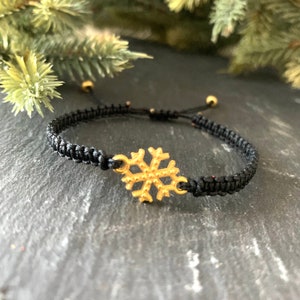 May include: A black braided bracelet with a gold snowflake charm.