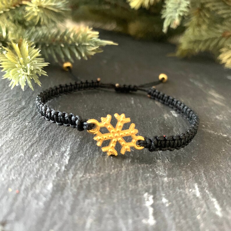 May include: A black braided bracelet with a gold snowflake charm.