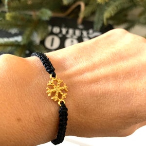 May include: A black braided bracelet with a gold snowflake charm.