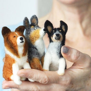 May include: Three needle felted dog figurines. The dogs are sitting and are brown and white, black and white, and gray and white.