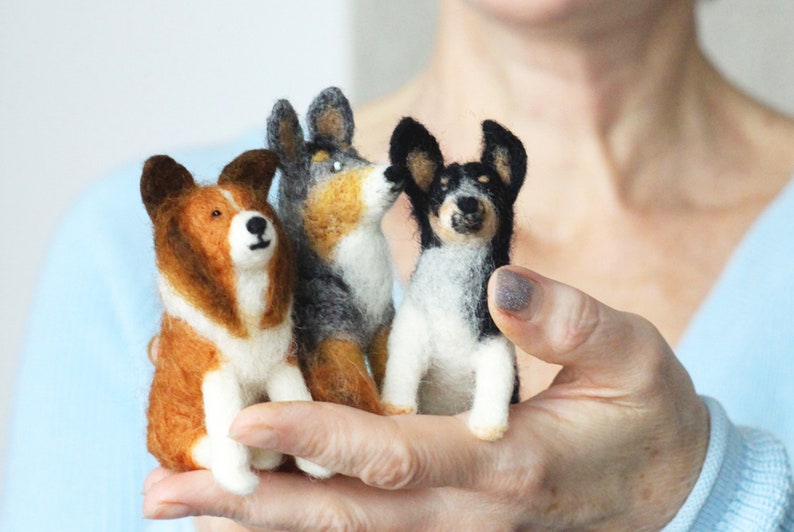 May include: Three needle felted dog figurines. The dogs are sitting and are brown and white, black and white, and gray and white.