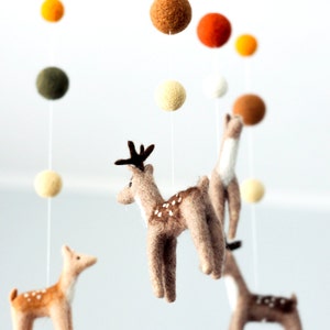 May include: A felt baby mobile with three brown deer, a white deer, and colorful felt balls. The deer are hanging from a wooden dowel.