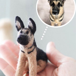 May include: A small, hand-felted German Shepherd dog figurine. The figurine is brown and black with a realistic appearance. It is being held in a person's hand.